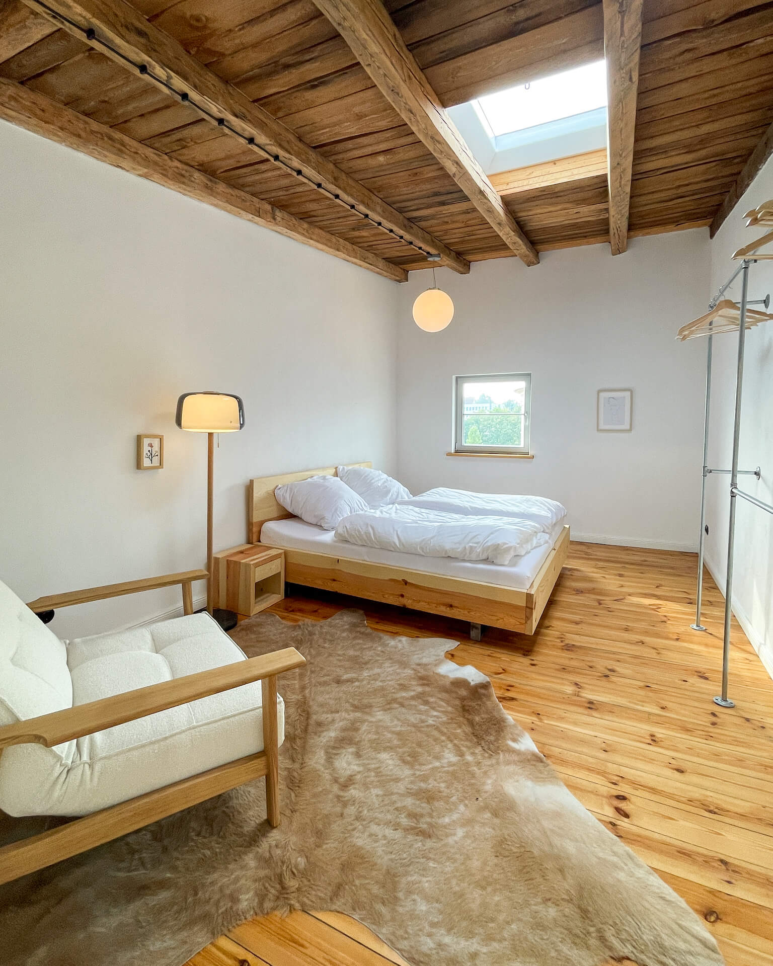 Massivholzbett mit schwebendem Design, Holzboden, Fellteppich, Holzstuhl und Dachfenster.