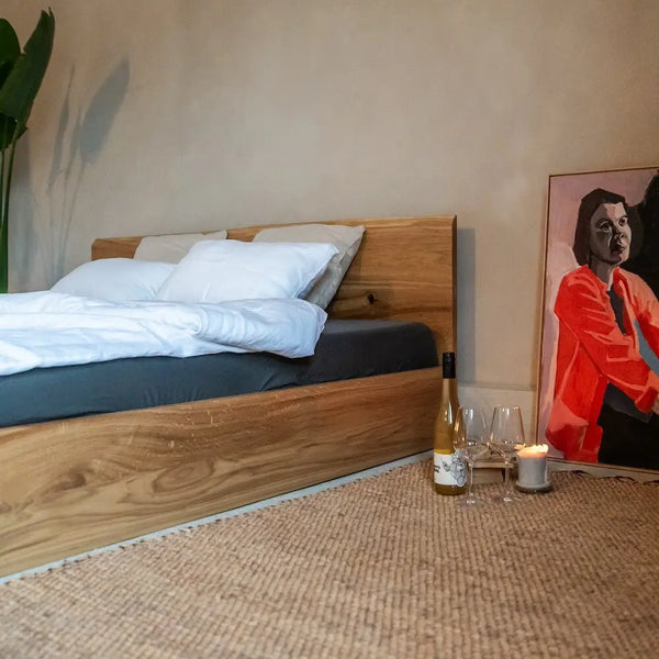 Eichenbett massiv mit Kopfteil, Kunstgemälde, Teppich, Weinflasche und Gläsern.