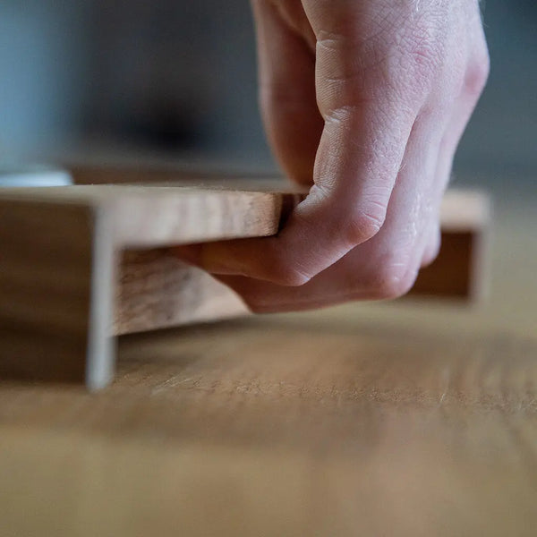 Hand greift filigrane Einkerbung eines Serviertabletts aus massiver Eiche mit klaren Linien.