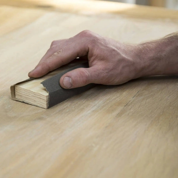 Hand schleift Massivholzmöbel mit Schleifklotz und Schleifpapier – optimale Vorbereitung für Reparatur und Pflege.