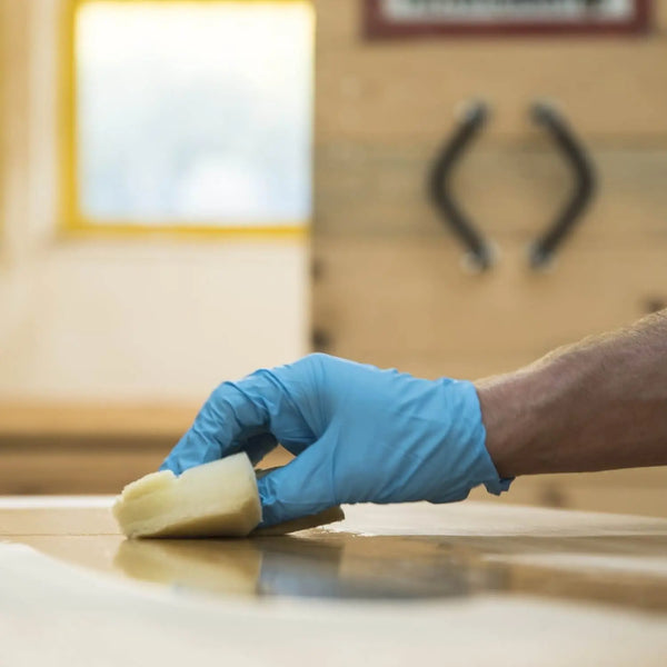 Holzpflege mit Pflegeset – Hand mit Handschuh trägt Hartwachs Öl mit Schwamm auf Massivholzmöbel auf, für Schutz und Langlebigkeit der Oberfläche.