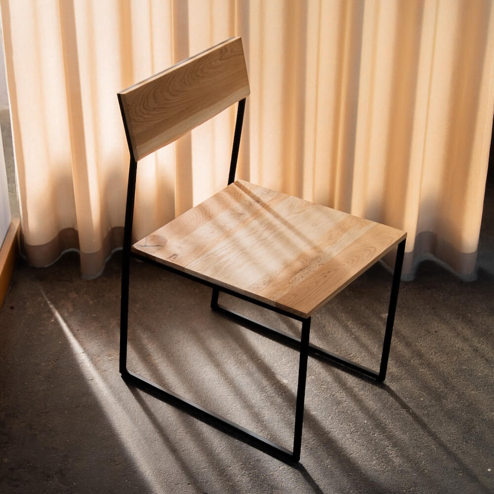Massivholzstuhl aus Eiche mit schwarzem Stahlgestell in natürlichem Licht, Design-Möbelstück
