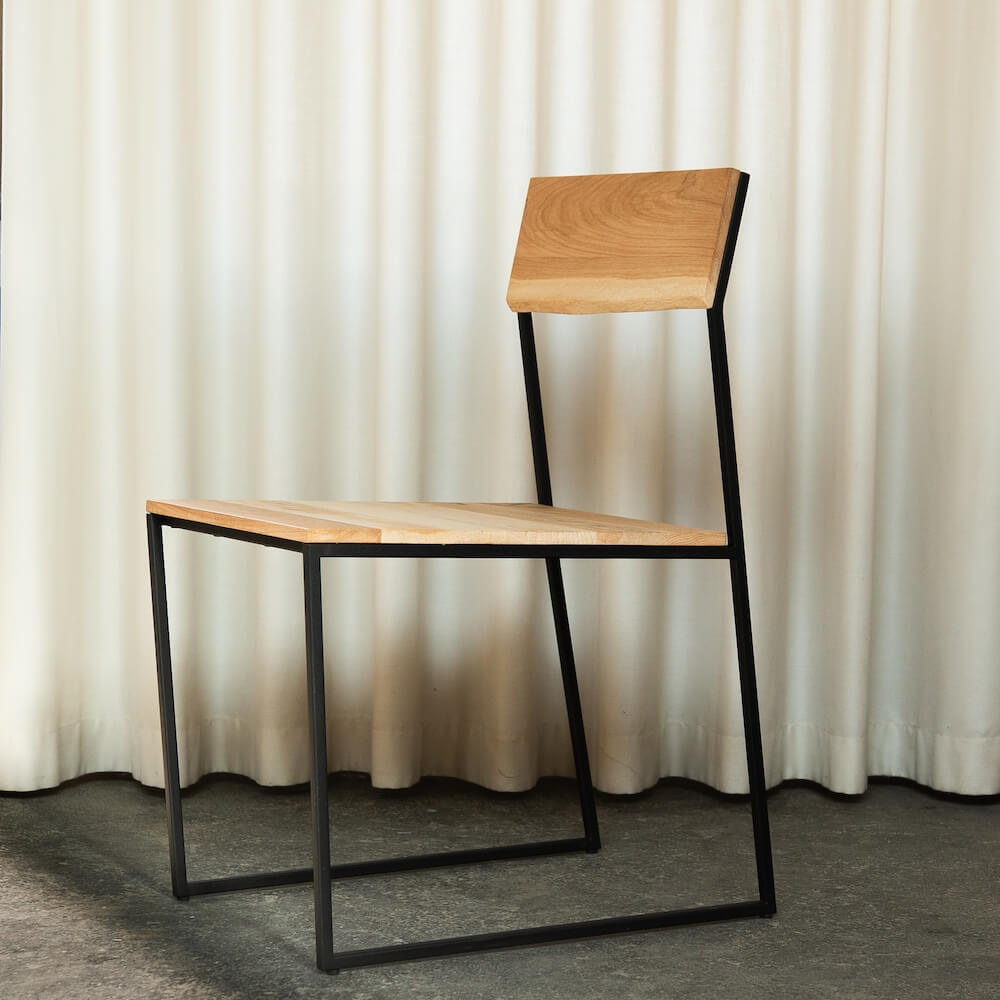 Stuhl MILO aus massiver Eiche mit schwarzem Stahlgestell vor Vorhang, nachhaltige Designmöbel Eiche